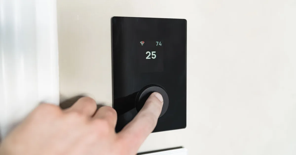 Hand beruehrt schwarzes KNX Smart Home Touchscreen-Thermostat an weisser Wand, Ratgeber von Rucker Elektro München