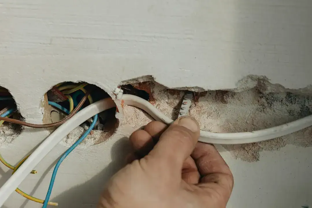 Hand zieht eine neue Leitung durch einen aufgestemmten Wandschlitz im Altbau, Ratgeber von Rucker Elektro München
