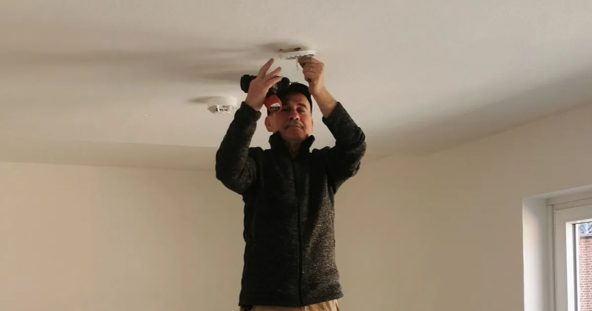 Fachmann montiert Rauchmelder an der Zimmerdecke einer Wohnung nach DIN 14676