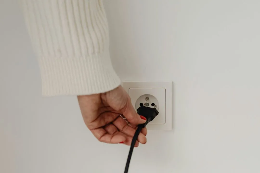 Hand zieht einen Stecker aus der Steckdose, um Stromkosten zu senken, Ratgeber von Rucker Elektro München