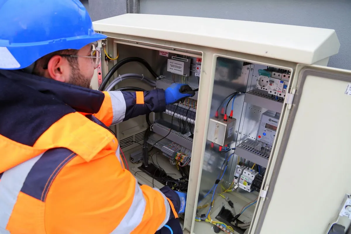 Elektroniker mit Helm, Schutzbrille und Isolierhandschuhen arbeitet an einer offenen Verteilung mit Sicherungsautomaten