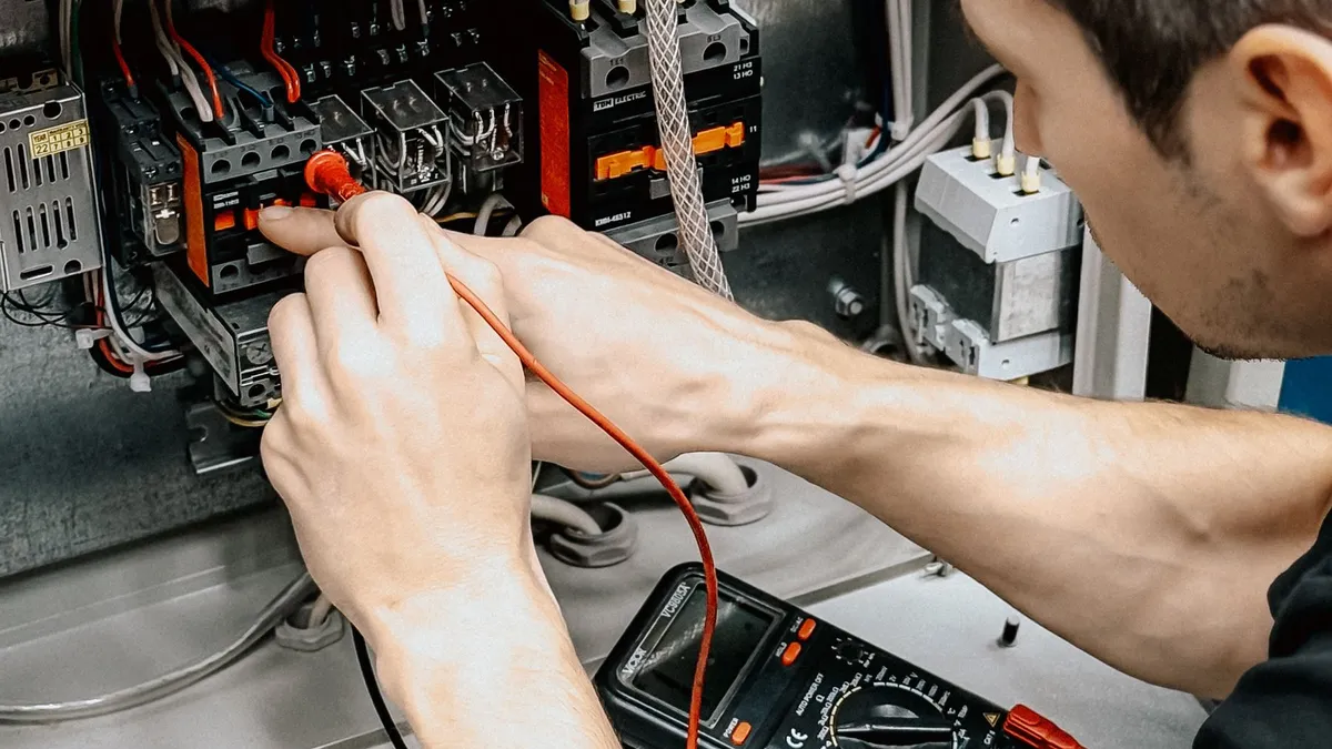 Elektriker misst beim E-Check in München mit Multimeter und Prüfspitzen an der offenen Verteilung