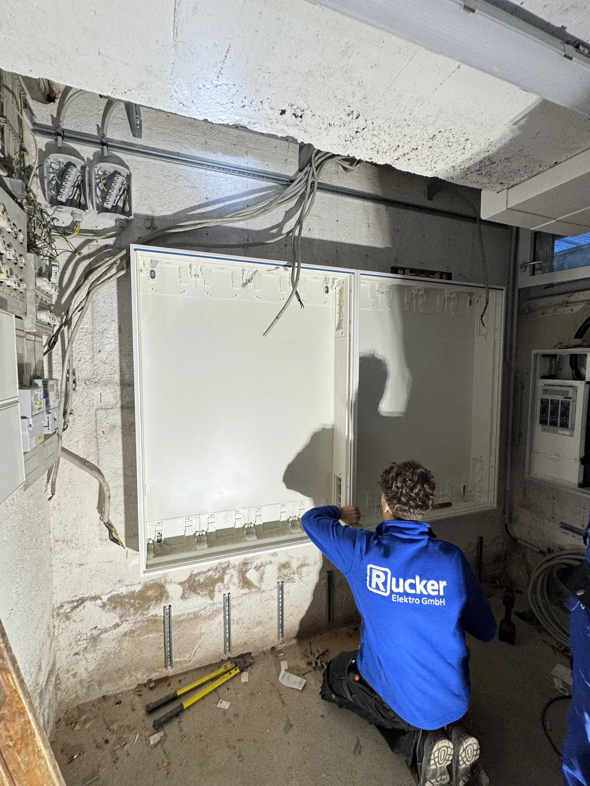 Monteur bei der Montage eines Zählerschrankgehäuses im Keller eines Münchner Mehrfamilienhauses