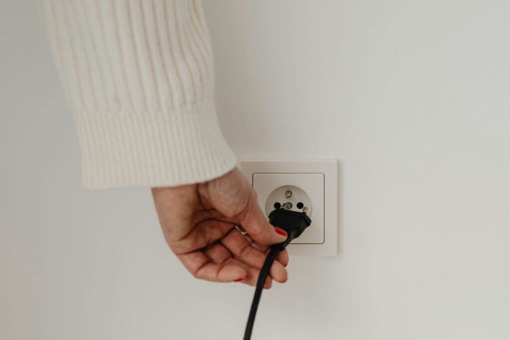 Hand steckt Kabel in eine Stromsteckdose, um Energie zu sparen.