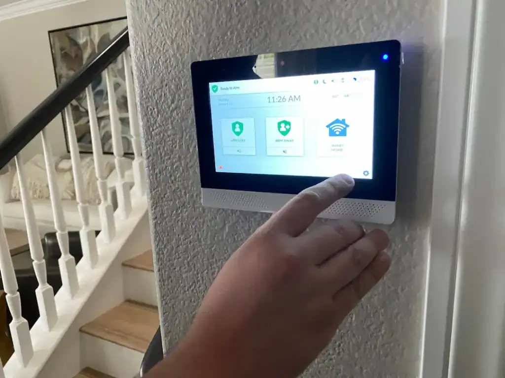 Hand aktiviert Alarmanlage über Wanddisplay im Hausflur.