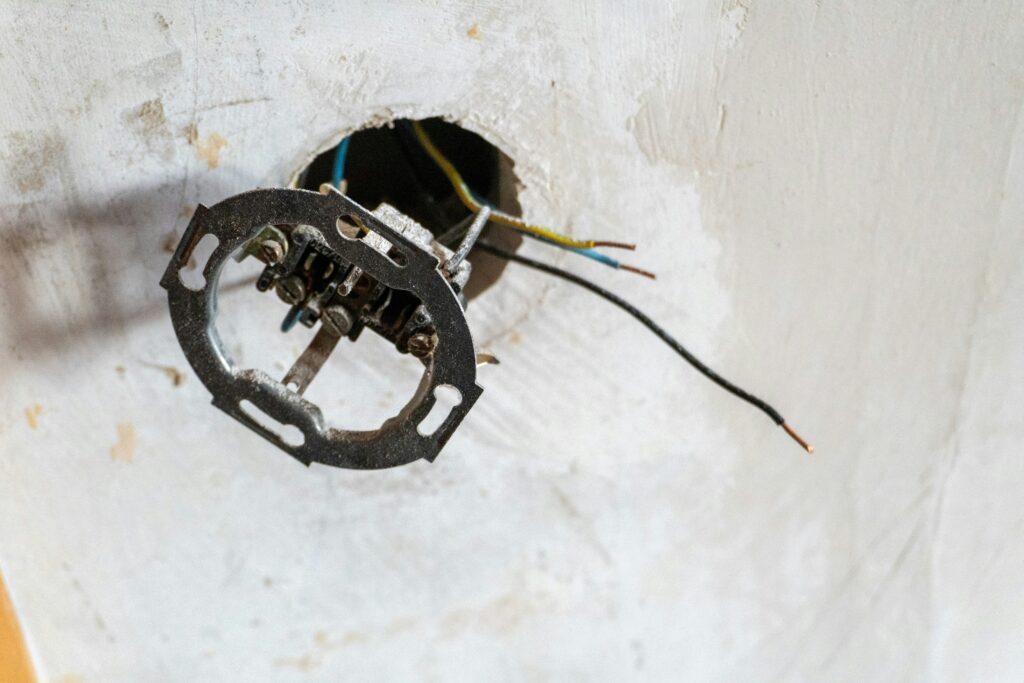 Eine freiliegende, unfertige Unterputz-Steckdose in einer Wand mit lose herabhängenden elektrischen Kabeln.