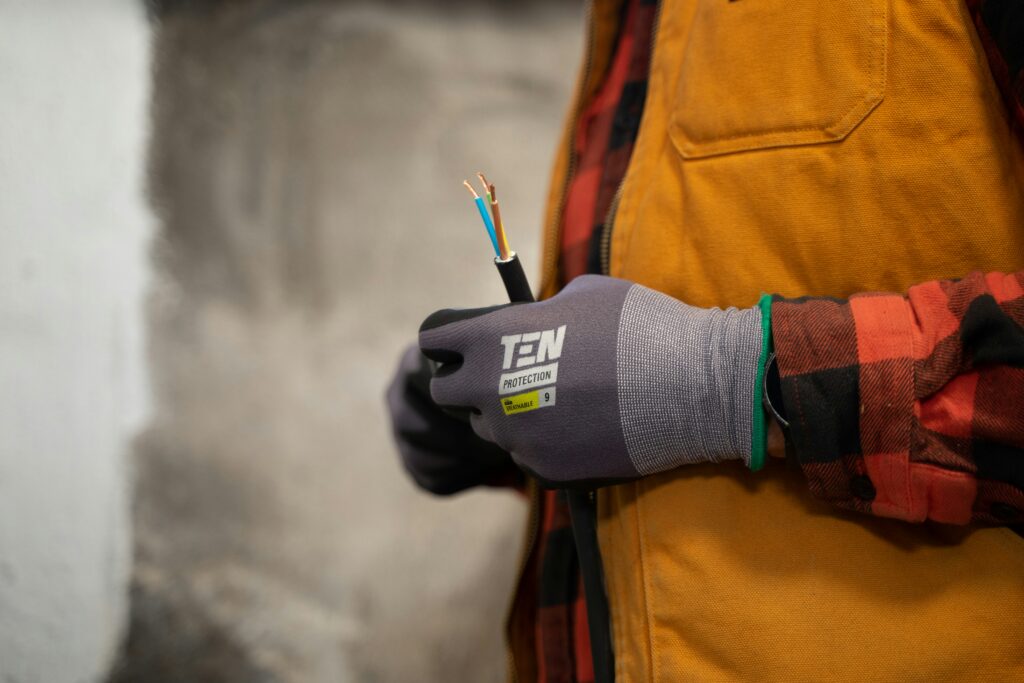 Elektriker mit Schutzhandschuhen hält ein abisoliertes Stromkabel mit freiliegenden Adern