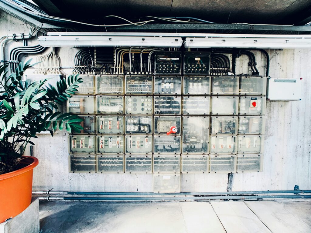 Große Wand mit mehreren transparenten Elektro-Verteilerkästen und Kabelführungen in einem Industriegebäude