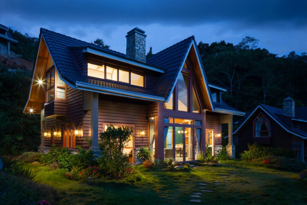 Beleuchtetes Holzchalet mit großen Glasfronten und gepflegtem Garten in der Abenddämmerung