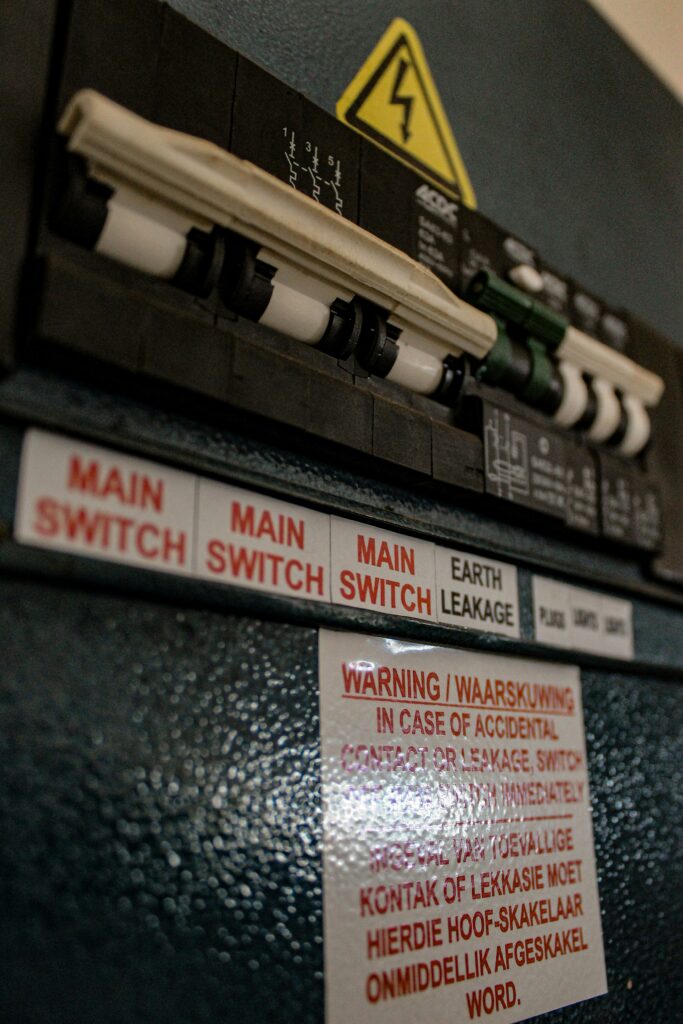 Alter Hauptschalter-Verteilerkasten mit Beschriftungen "Main Switch" und "Earth Leakage" sowie zweisprachigem Warnhinweis auf Englisch und Afrikaans zu Stromschlaggefahr