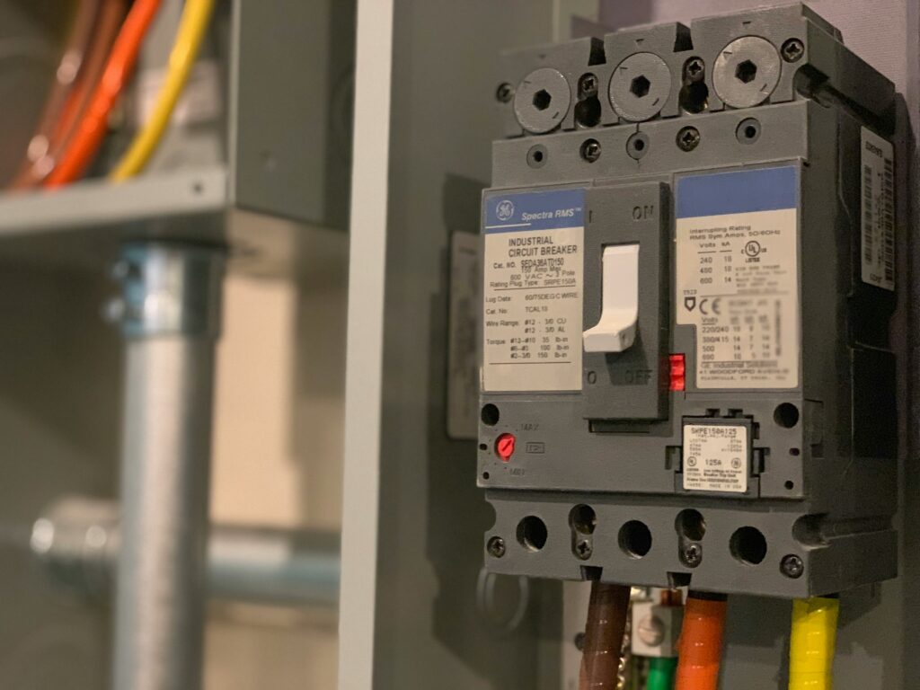Grauer industrieller GE Spectra RMS Leistungsschalter (150 A) mit weißem Kippschalter in Aus-Stellung und braunen, orangen und gelben Anschlusskabeln